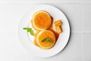 Photo of Tasty puddings with caramel sauce served on white tiled table, top view