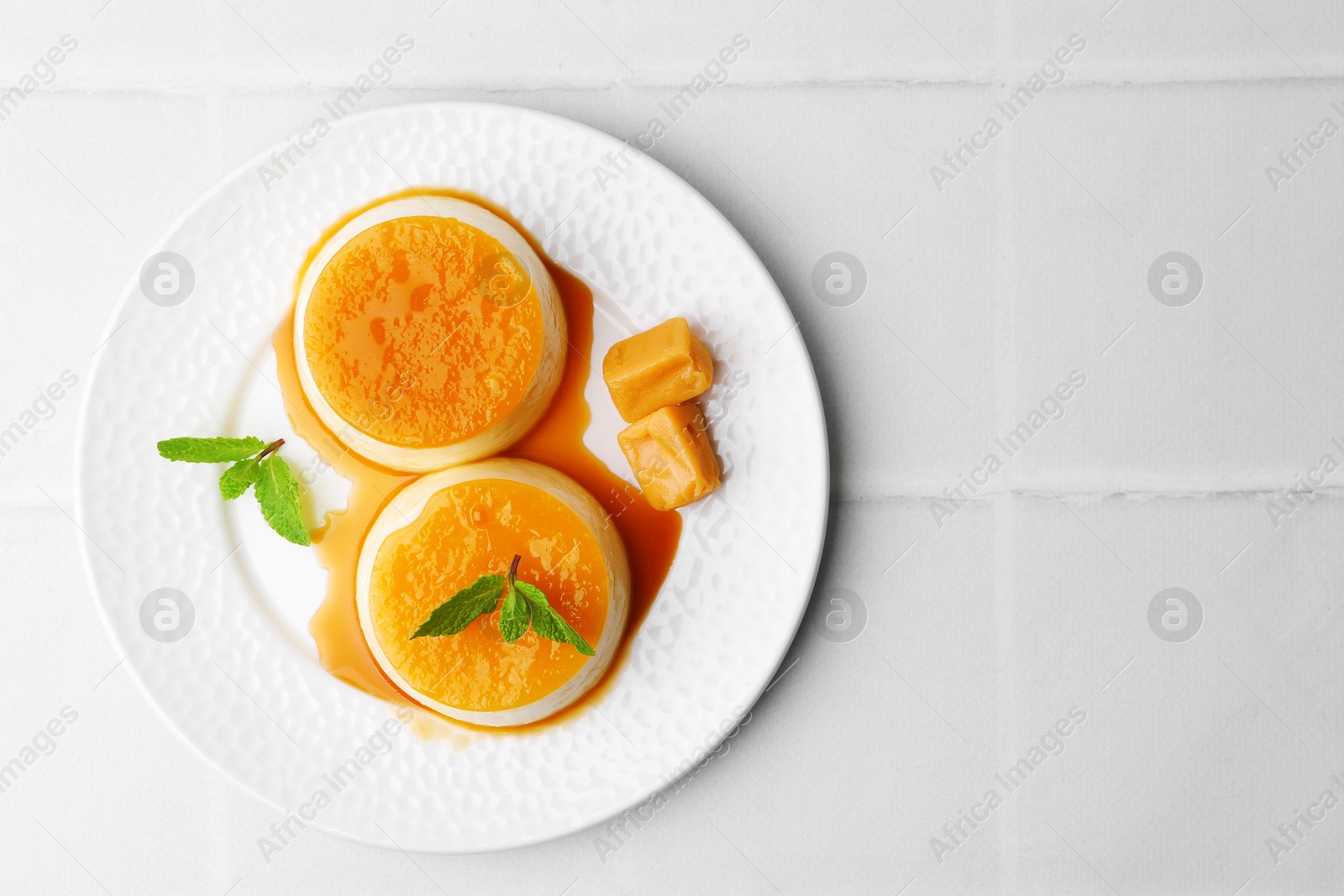 Photo of Tasty puddings with caramel sauce served on white tiled table, top view. Space for text