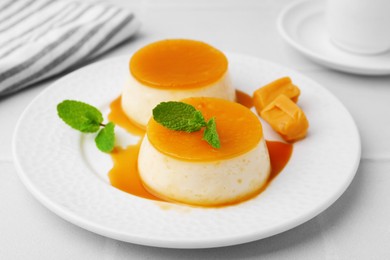 Photo of Tasty puddings with caramel sauce served on white tiled table, closeup