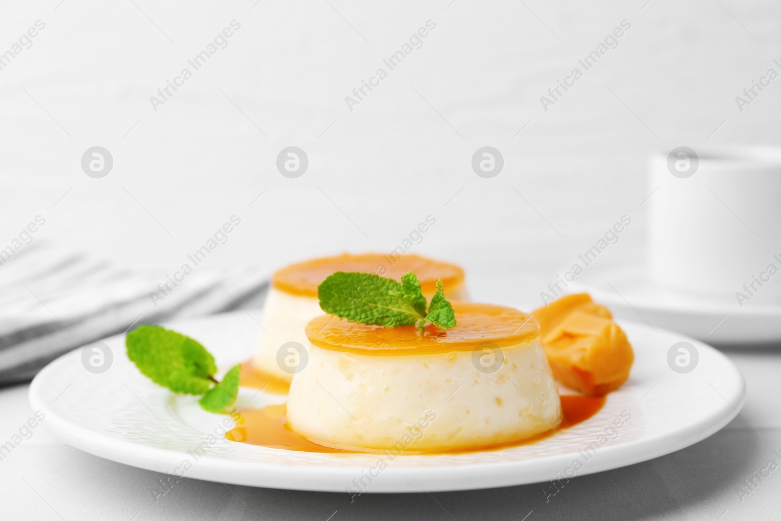 Photo of Tasty puddings with caramel sauce served on white tiled table, closeup