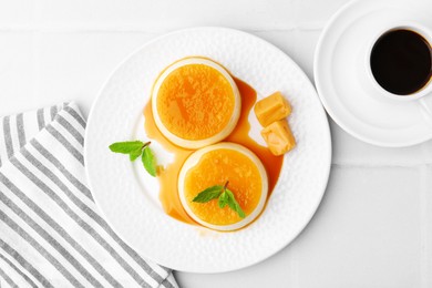 Photo of Tasty puddings with caramel sauce served on white tiled table, top view