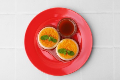 Photo of Tasty puddings with caramel sauce served on white tiled table, top view