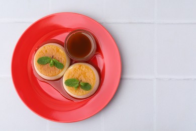 Photo of Tasty puddings with caramel sauce served on white tiled table, top view. Space for text