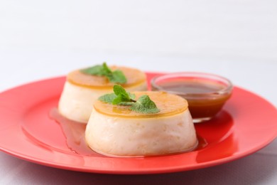 Photo of Tasty puddings with caramel sauce served on white tiled table, closeup