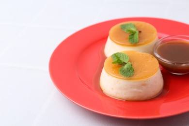 Photo of Tasty puddings with caramel sauce served on white tiled table, closeup. Space for text