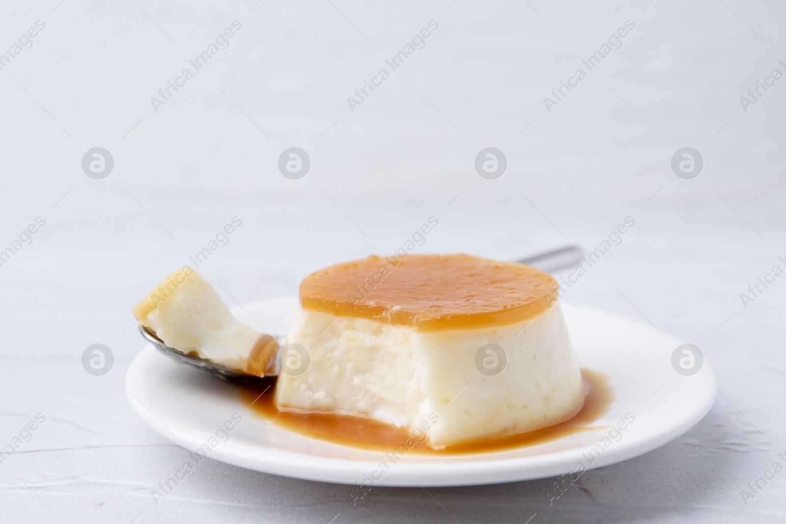 Photo of Tasty pudding with caramel sauce served on white textured table, closeup. Space for text