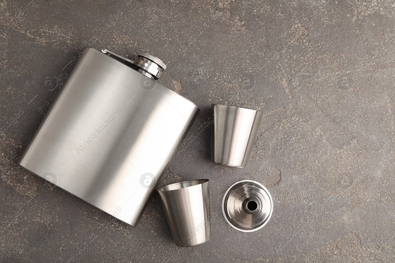 Photo of Hip flask, cups and funnel on grey table, flat lay. Space for text