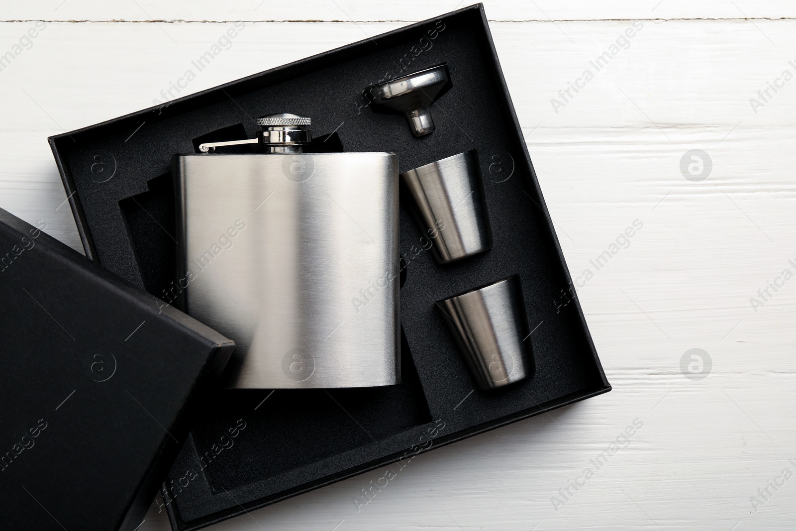 Photo of Hip flask, cups and funnel in package on white wooden table, top view. Space for text