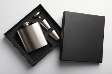 Photo of Hip flask, cups and funnel in package on white background, top view