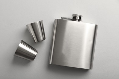 Photo of Hip flask and cups on white background, flat lay