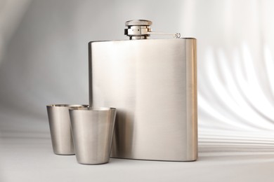 Photo of Hip flask and cups on light table, closeup