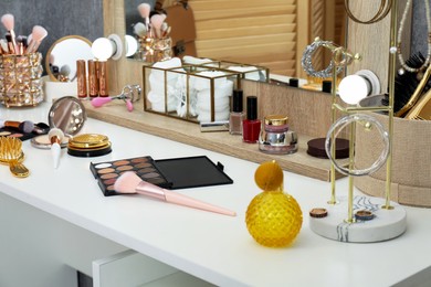 Photo of Makeup room. Mirror, different beauty products and jewelry on white dressing table indoors