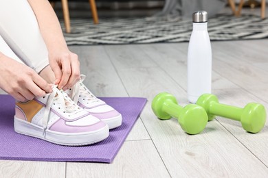 Photo of Woman tying shoelaces and gym equipment indoors, closeup