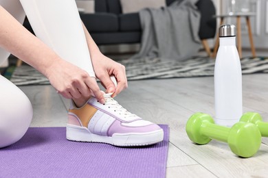 Photo of Woman tying shoelaces and gym equipment indoors, closeup