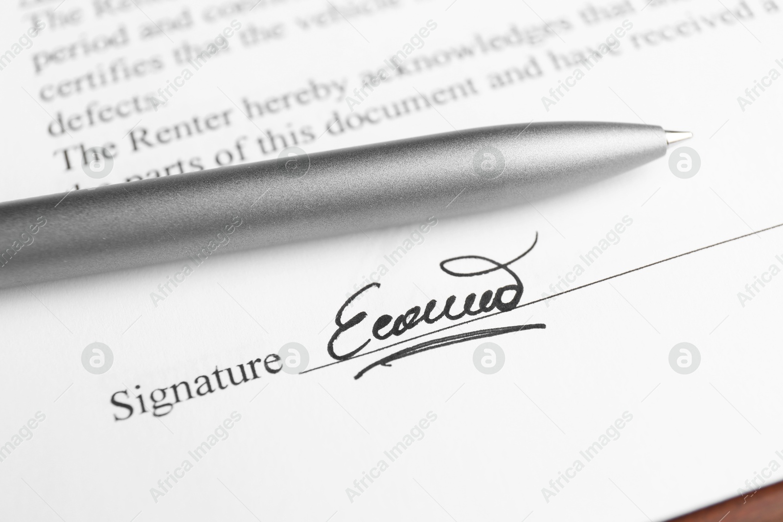 Photo of Ballpoint pen and signature on contract at wooden table, closeup