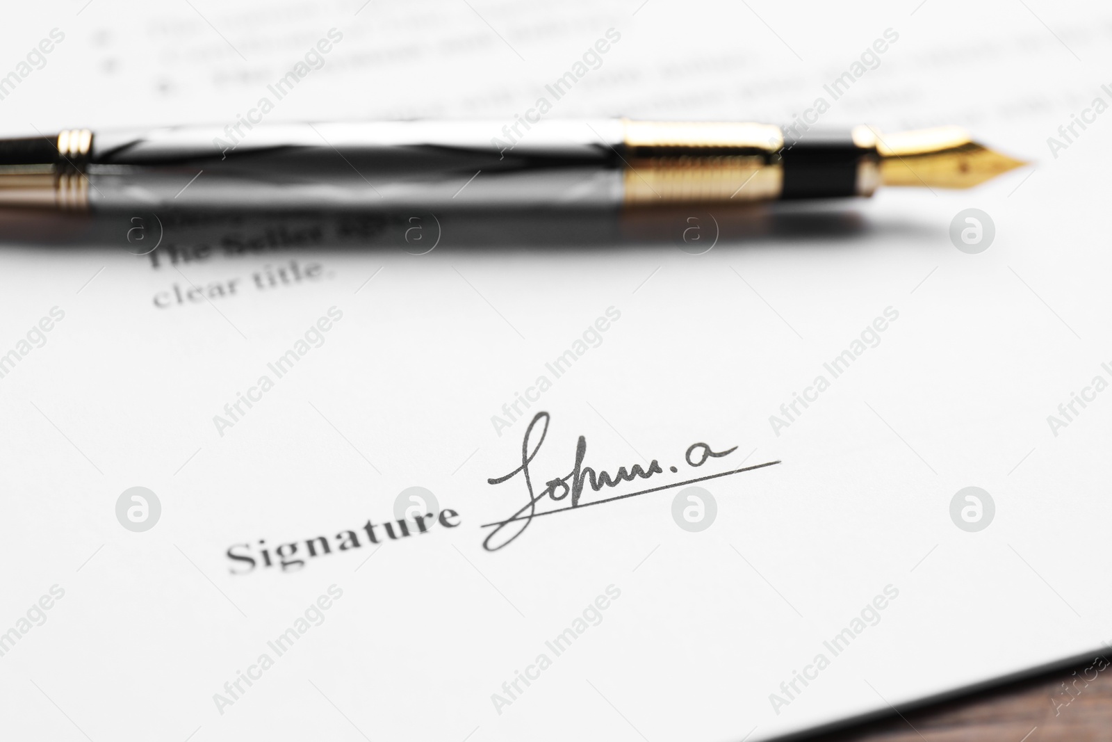 Photo of Fountain pen and signature on contract at wooden table, closeup