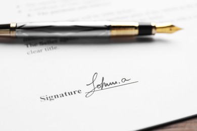 Photo of Fountain pen and signature on contract at wooden table, closeup