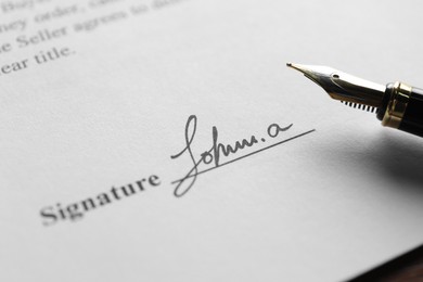 Photo of Fountain pen and signature on contract at wooden table, closeup