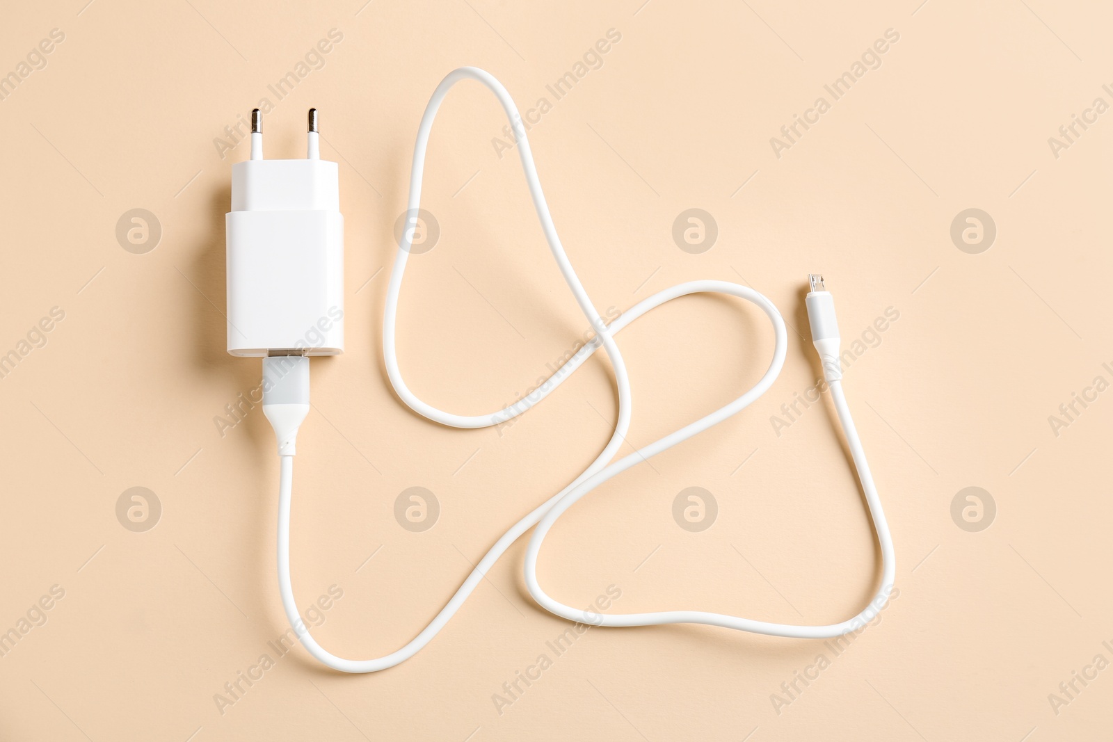 Photo of USB power adapter with charge cable on beige background, top view