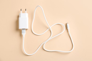 Photo of USB power adapter with charge cable on beige background, top view