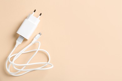 Photo of USB power adapter with charge cable on beige background, top view. Space for text