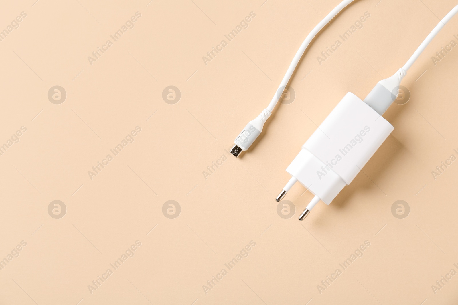 Photo of USB power adapter with charge cable on beige background, top view. Space for text