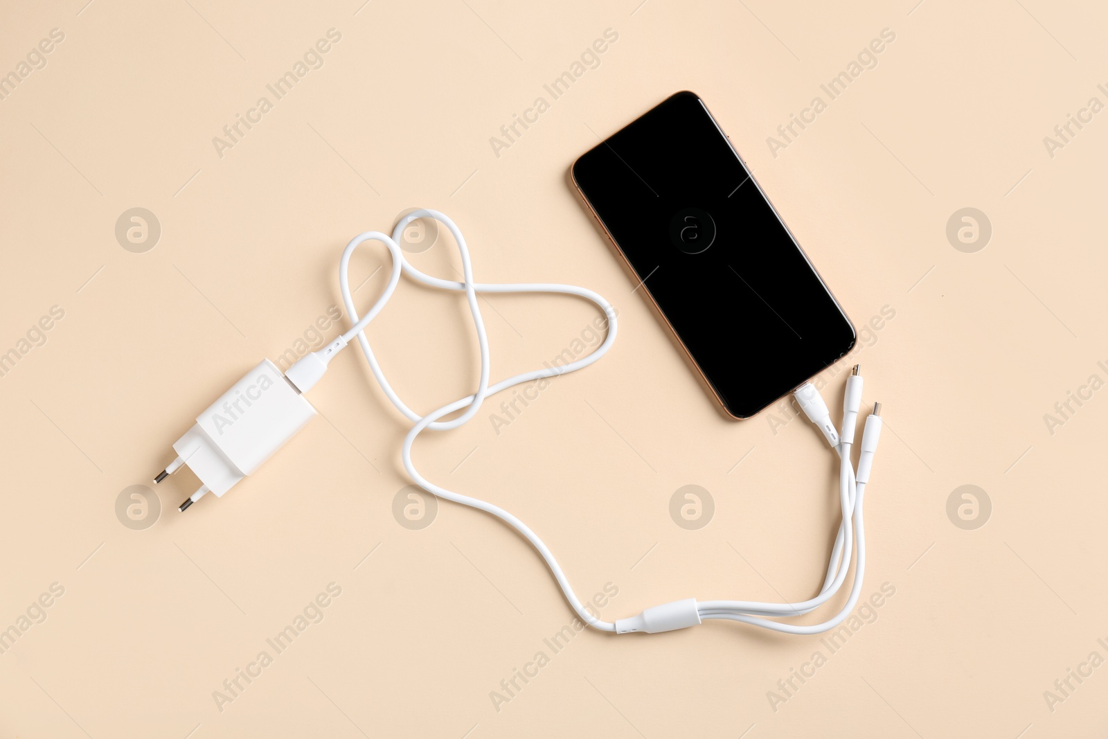 Photo of Triple charge cable connected to smartphone on beige background, top view