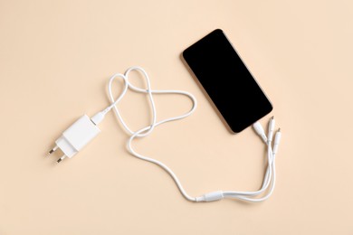 Photo of Triple charge cable connected to smartphone on beige background, top view