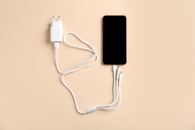 Photo of Triple charge cable connected to smartphone on beige background, top view