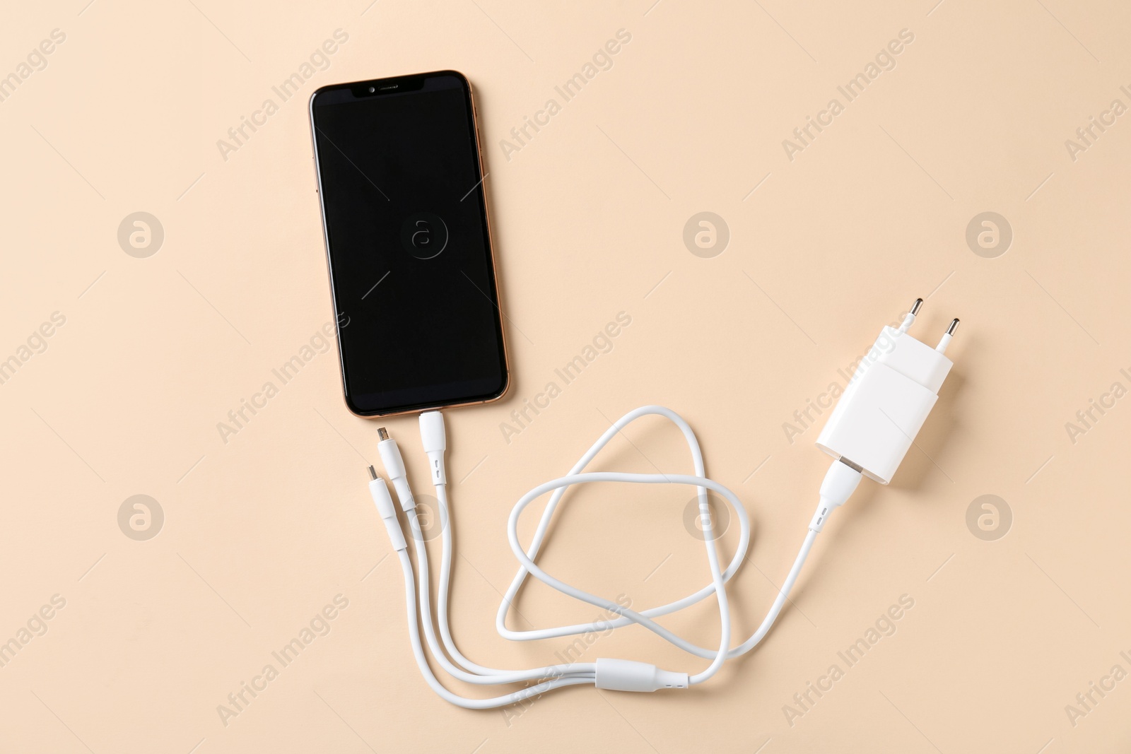 Photo of Triple charge cable connected to smartphone on beige background, top view