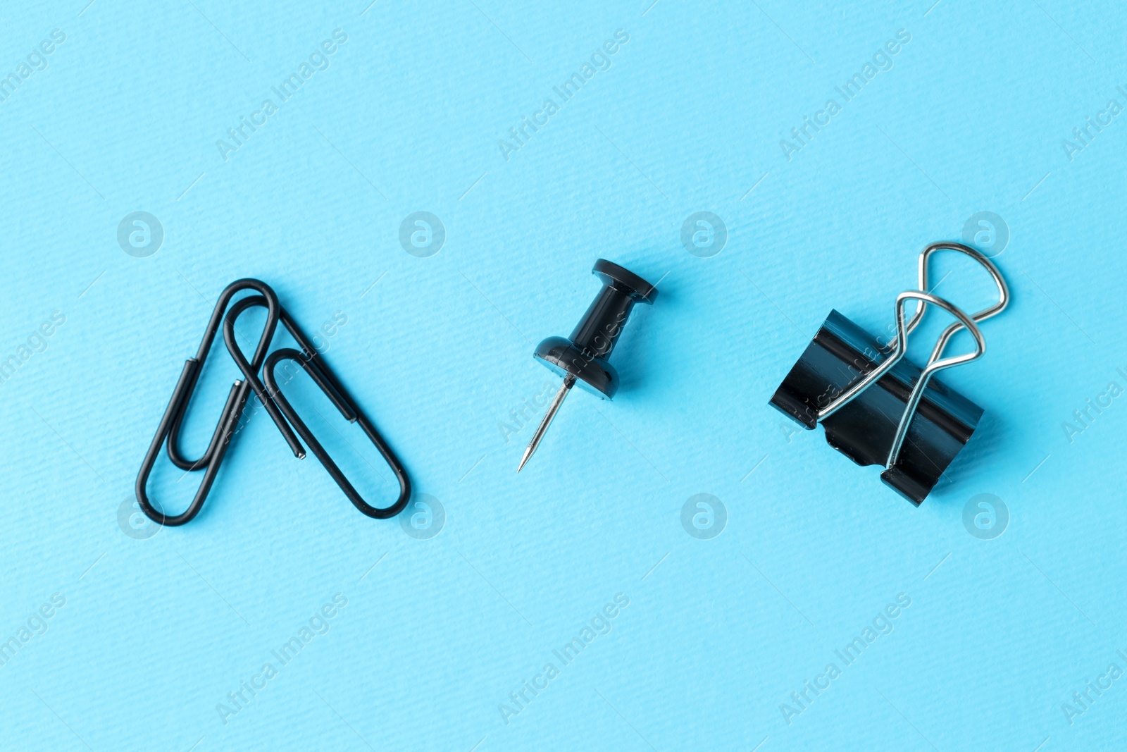 Photo of Paper clips and pin on light blue background, flat lay