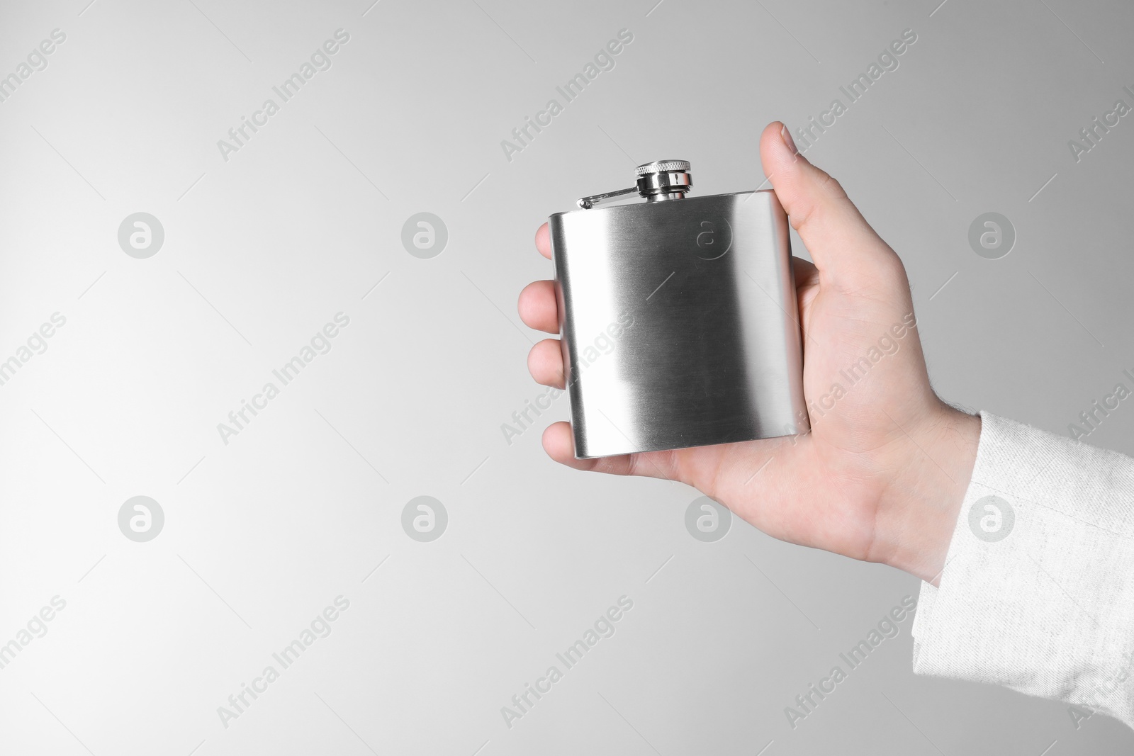 Photo of Man holding metal hip flask on light grey background, closeup. Space for text