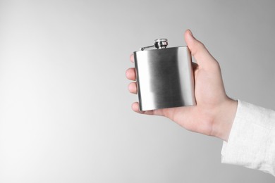 Photo of Man holding metal hip flask on light grey background, closeup. Space for text