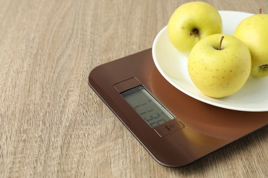 Photo of Modern electronic kitchen scale with apples on wooden table, closeup. Space for text