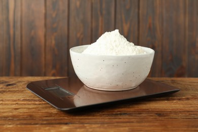 Photo of Modern electronic kitchen scale with bowl of flour on wooden table, closeup