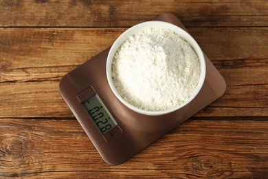 Photo of Modern electronic kitchen scale with bowl of flour on wooden table, top view