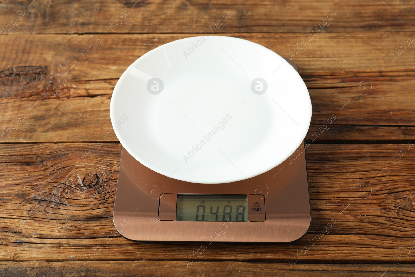 Photo of Modern electronic kitchen scale with plate on wooden table, closeup