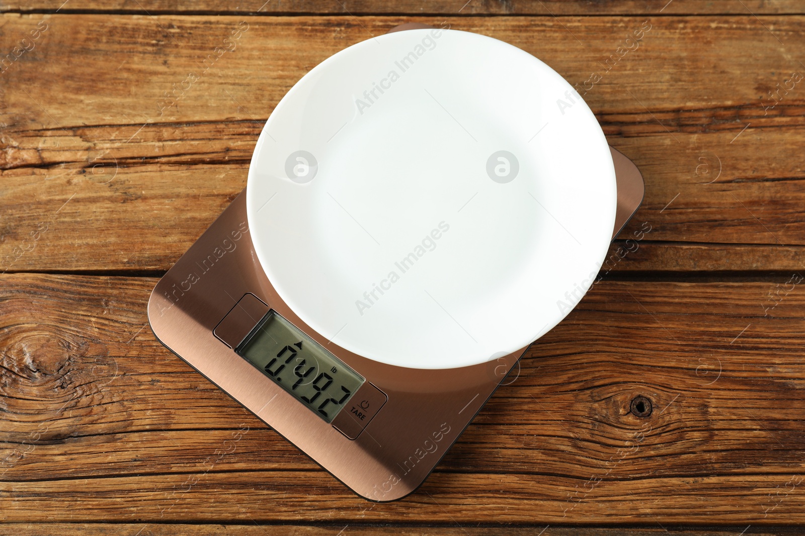 Photo of Modern electronic kitchen scale with plate on wooden table, above view