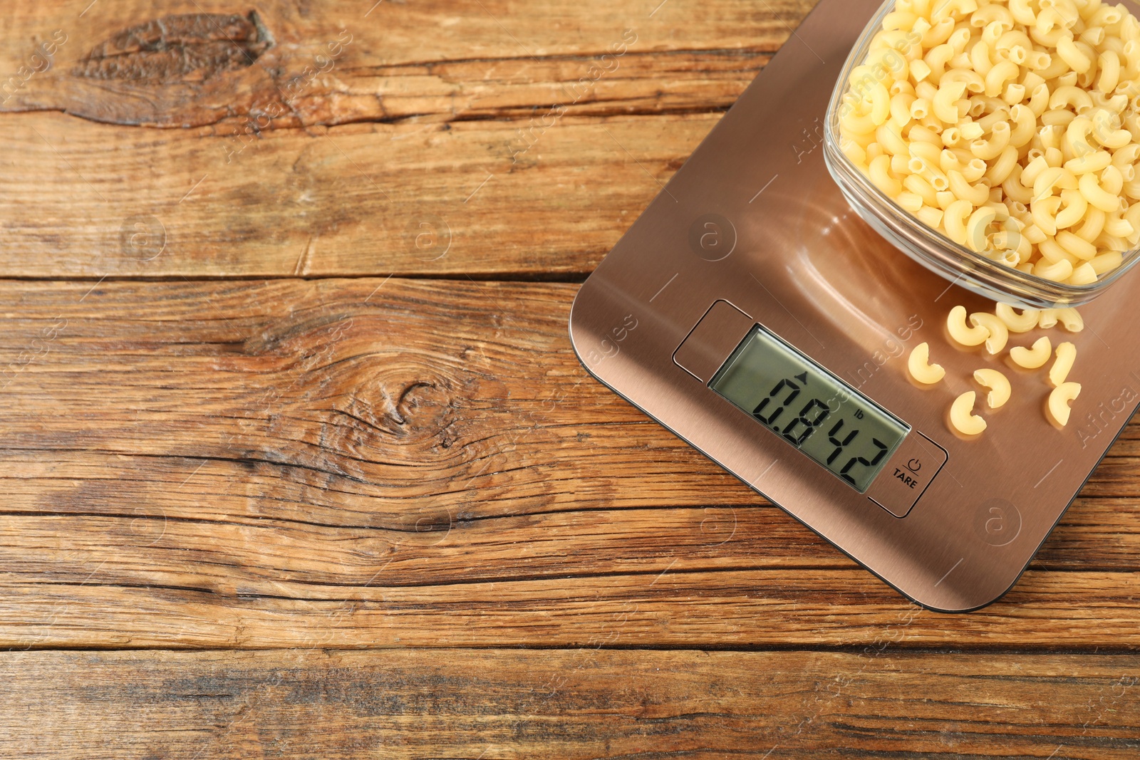 Photo of Modern electronic kitchen scale with bowl of raw pasta on wooden table, top view. Space for text