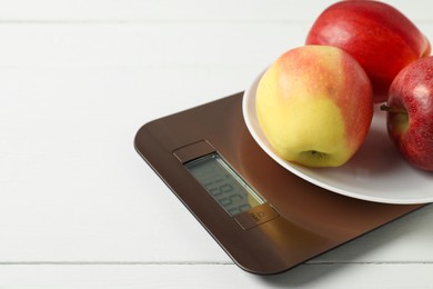 Photo of Modern electronic kitchen scale with apples on white wooden table, closeup. Space for text