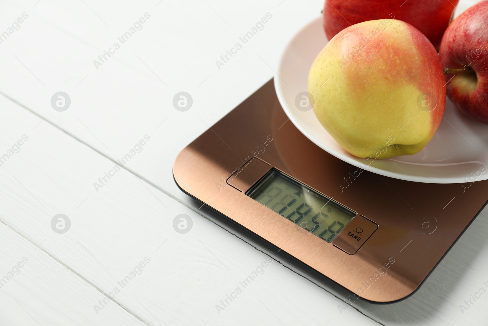 Photo of Modern electronic kitchen scale with apples on white wooden table, closeup. Space for text