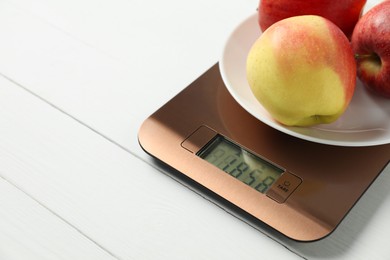 Photo of Modern electronic kitchen scale with apples on white wooden table, closeup. Space for text