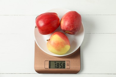 Photo of Modern electronic kitchen scale with apples on white wooden table, top view