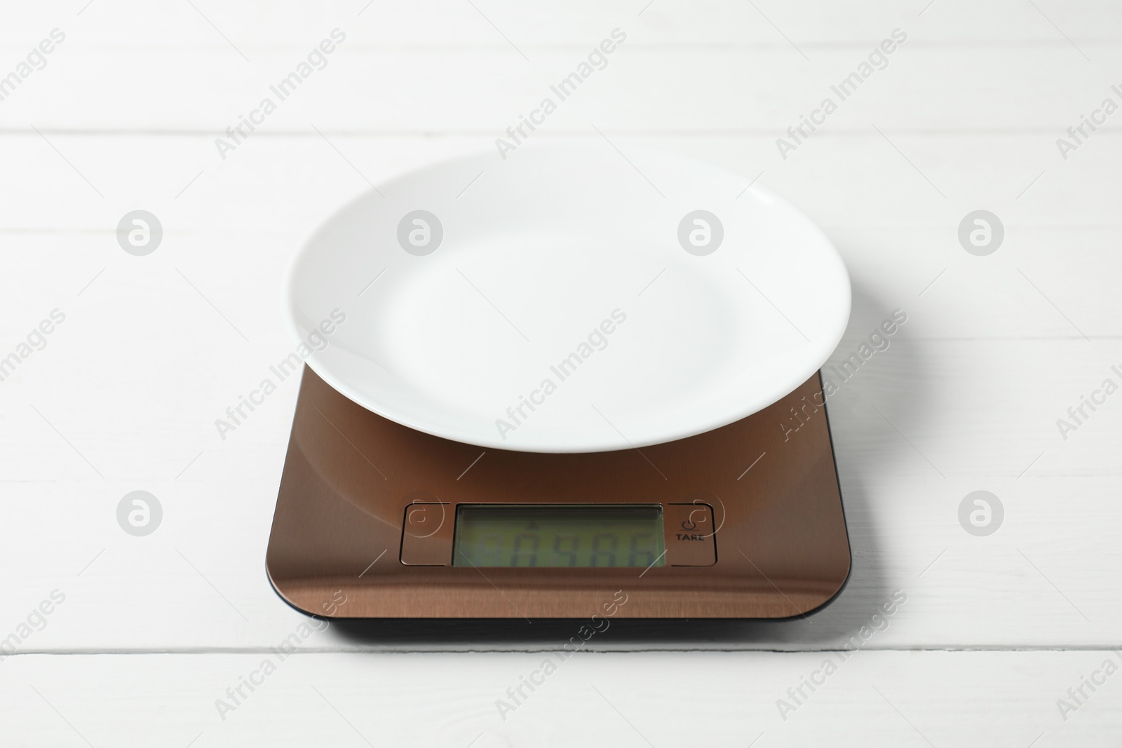 Photo of Modern electronic kitchen scale with plate on white wooden table, closeup