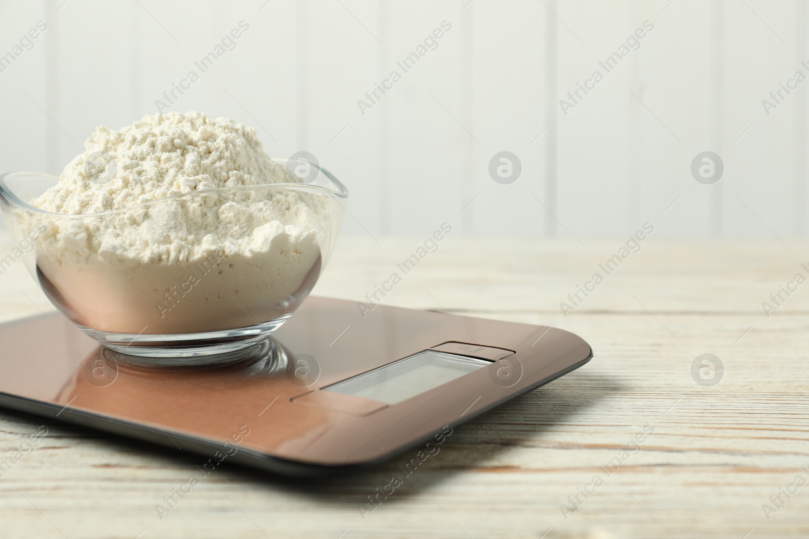 Photo of Modern electronic kitchen scale with bowl of flour on wooden table, closeup. Space for text