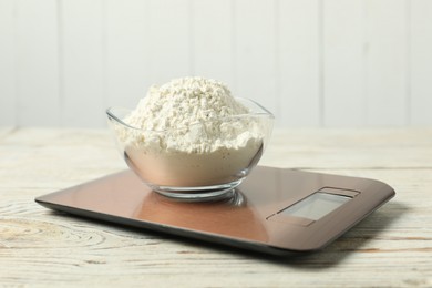 Photo of Modern electronic kitchen scale with bowl of flour on wooden table, closeup