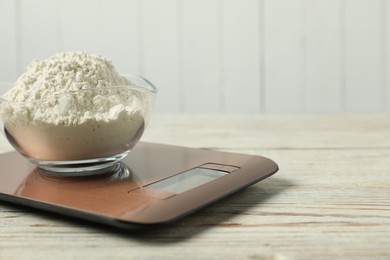 Photo of Modern electronic kitchen scale with bowl of flour on wooden table, closeup. Space for text