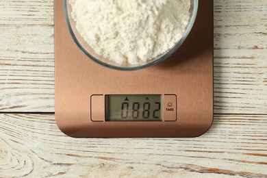 Photo of Modern electronic kitchen scale with bowl of flour on wooden table, top view