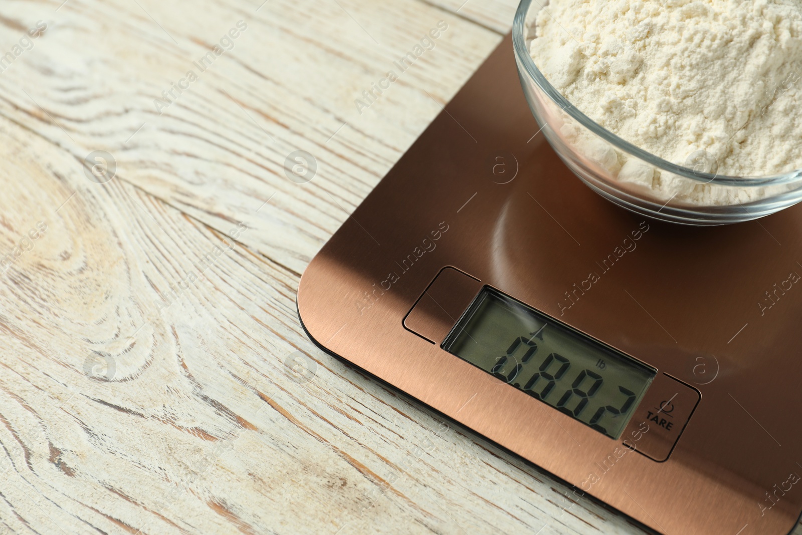 Photo of Modern electronic kitchen scale with bowl of flour on wooden table, closeup. Space for text