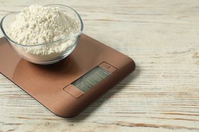 Photo of Modern electronic kitchen scale with bowl of flour on wooden table, closeup. Space for text